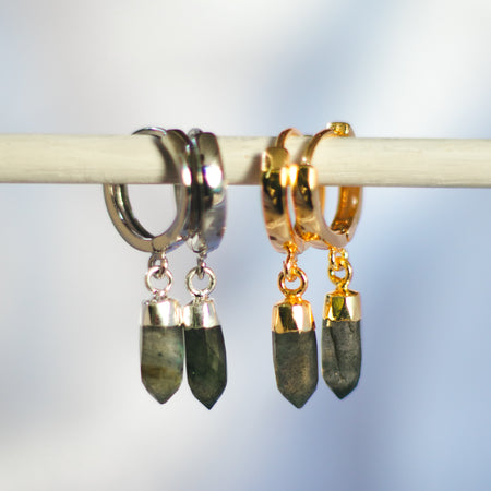 Two pairs of hoop earrings with dangling gemstones on a blurred background